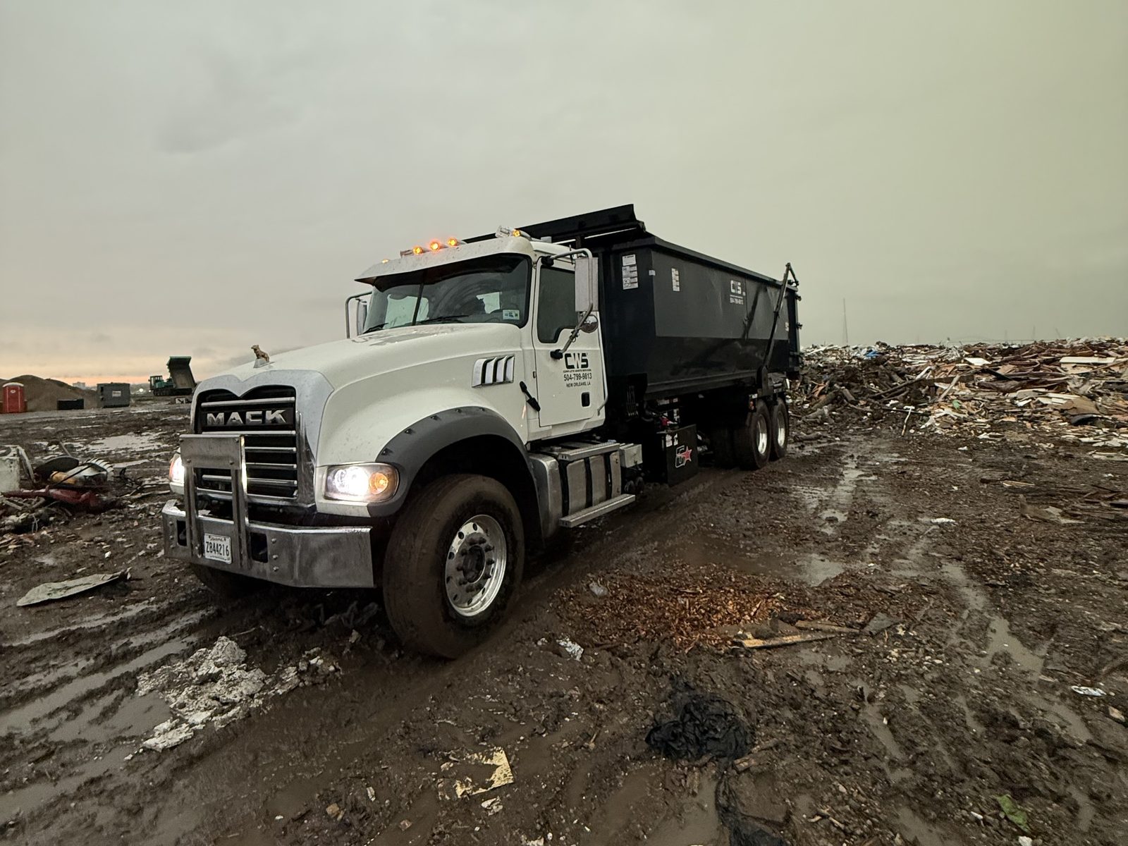 A Complete Waste Services roll-off truck delivering a dumpster at a job site